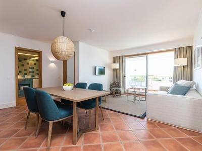 Světý obývací prostor s jídelním stolem, modrými židlemi a pohovkou u velkých oken s výhledem.