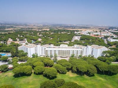 Velká bílá hotelová budova obklopená zelenými stromy a golfovým hřištěm pod jasnou oblohou.