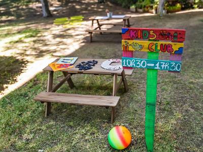 Barevné dětské hřiště s piknikovým stolem, jasným míčem a cedulí ve stínu stromu.