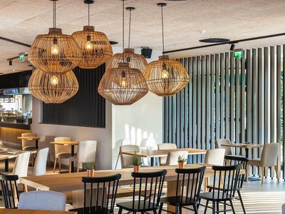 Světlá restaurace s dřevěnými židlemi, stoly a kulatými bambusovými lampami zavěšenými u stropu.