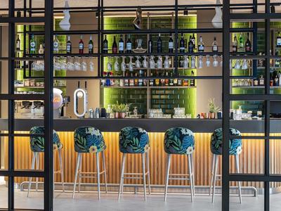 Moderner Hotelbarbereich mit stilvollen Barhockern und beleuchteten Regalen voller Flaschen.