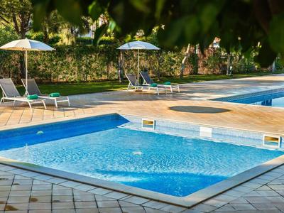 Dva bazény s čistou vodou, obklopené lehátky a slunečníky na zahradě.