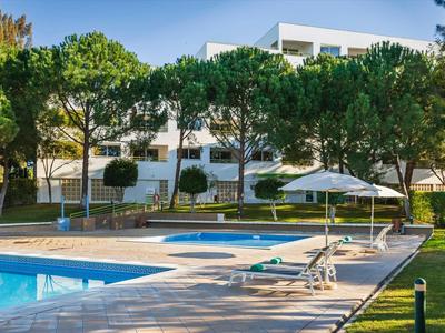 Moderní bazénová oblast s lehátky a slunečníkem v hotelovém komplexu.