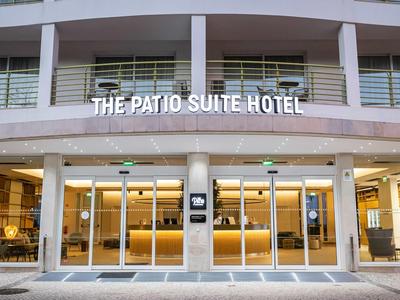 Eingangsbereich des The Patio Suite Hotels mit moderner Glasfassade und beleuchtetem Schild.