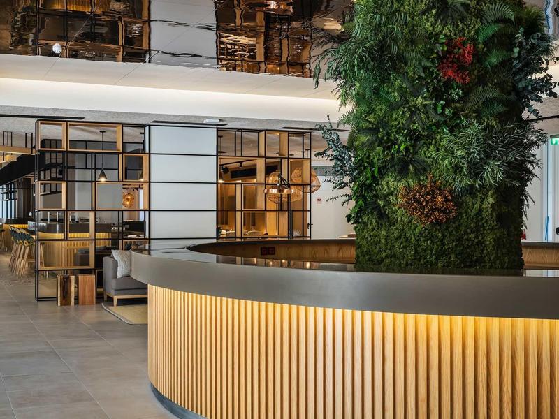 Moderní hotelová hala s kulatou recepcí a velkou zelenou rostlinou.