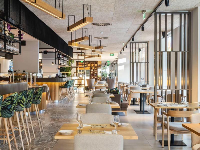 Moderní restaurace se světlým dřevěným nábytkem a rostlinami u baru.