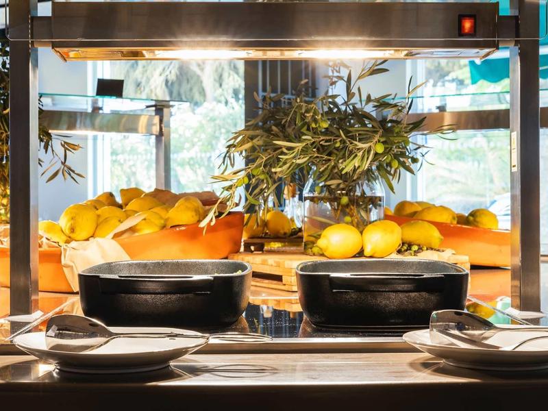 Čerstvé ovoce a pečivo na bufetovém pultu v jasné restauraci s přirozeným světlem.