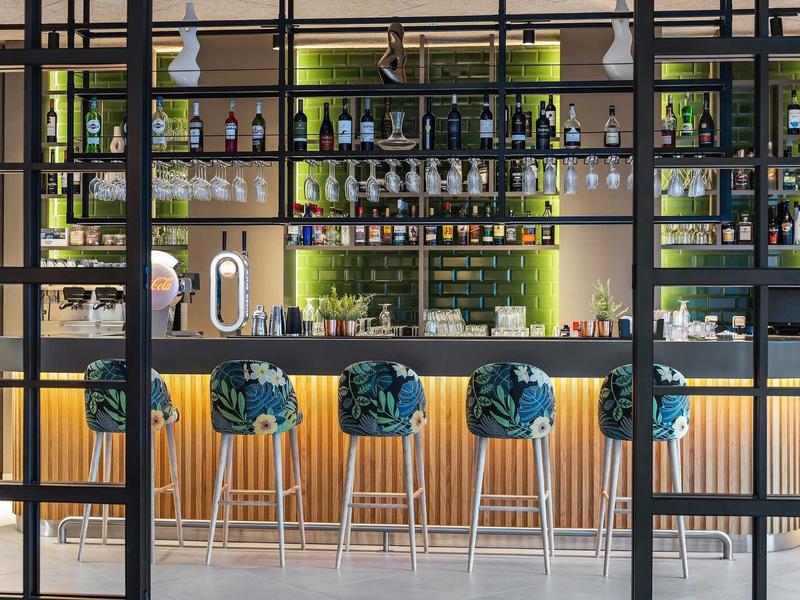 Moderní hotelový bar s zelenými barovými židlemi a osvětlenými regály plnými lahví.