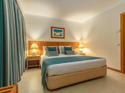 Dormitorio con cama doble, cortinas azul-verde, dos mesas de noche y luz cálida.