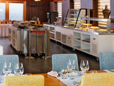 Buffet de desayuno en un restaurante de hotel con mesas y sillas modernas y bandejas de comida.