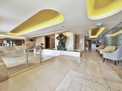 Gran vestíbulo de hotel con iluminación moderna en el techo, área de descanso y mostrador de recepción.