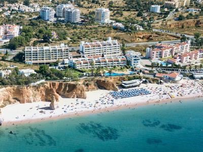 Vista aérea de un resort con playa, piscinas y paisaje circundante junto al mar.