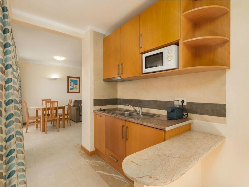 Pequeña cocina con armarios de madera y microondas en un apartamento de vacaciones con vista al comedor.