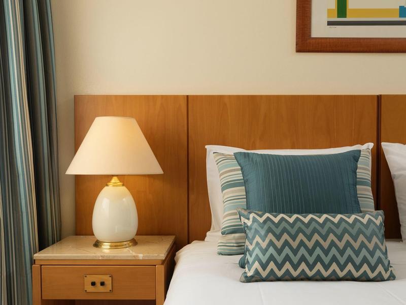 Dormitorio moderno con fondo de madera, lámpara de noche y cojines decorativos en la cama.