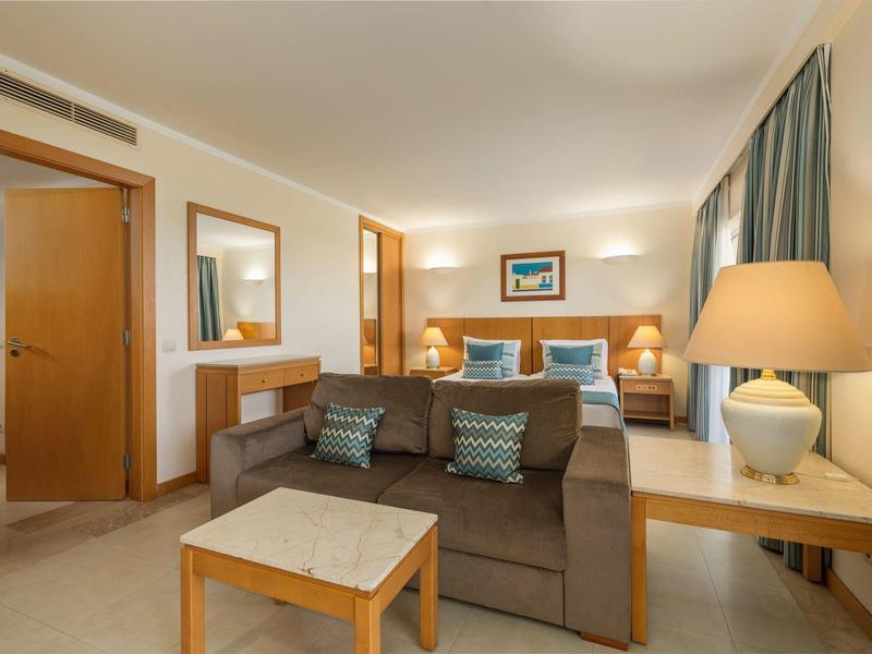 Cómoda habitación de hotel con sofá, camas, mesas de noche y luz cálida.