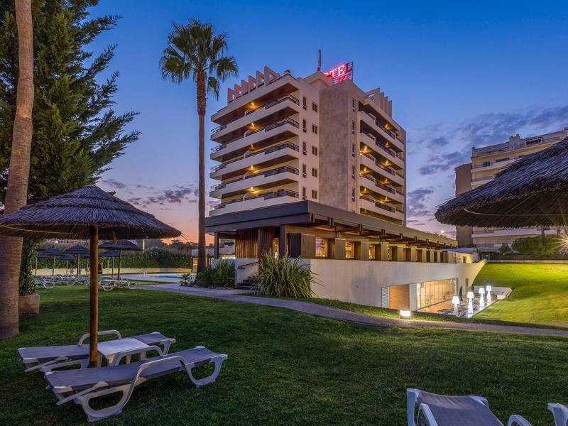 Edificio de hotel al anochecer con tumbonas y palmeras en un césped cuidado