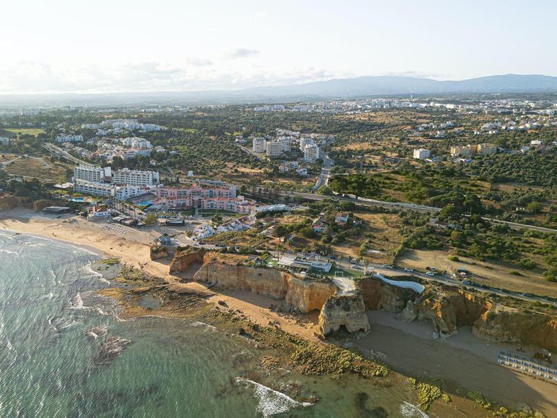 Vista aérea de una ciudad costera con playa, rocas y varios edificios en un entorno verde.
