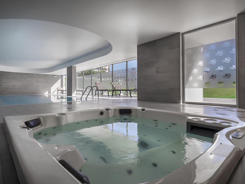 Jacuzzi interior moderno con ventana grande y luz natural en un spa de hotel.