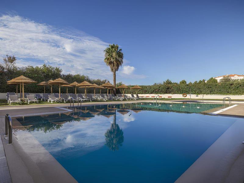 Piscina al aire libre con sombrillas y tumbonas bajo un cielo despejado en un hotel.