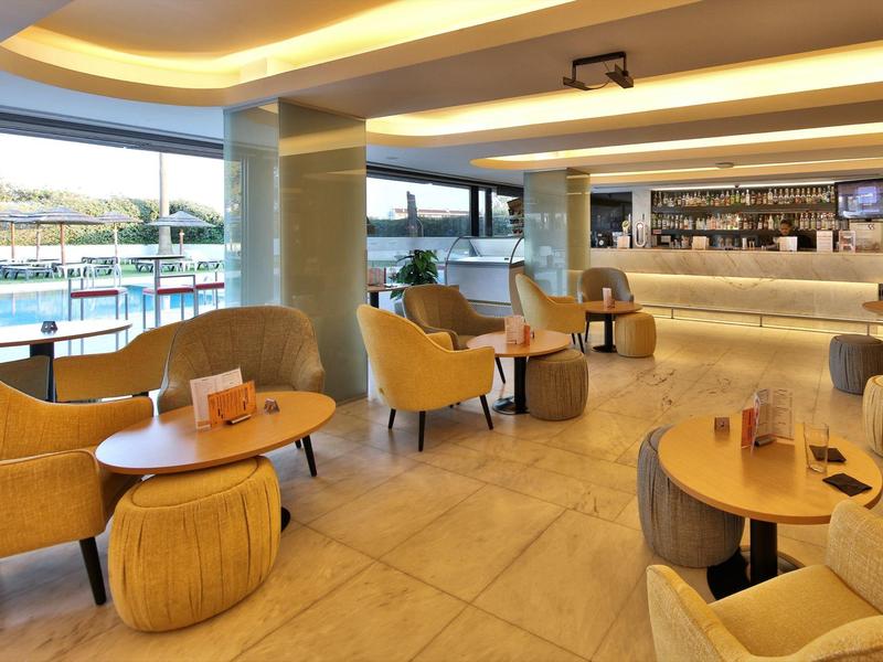 Área moderna del vestíbulo del hotel con sillones amarillos y vista a la piscina exterior.