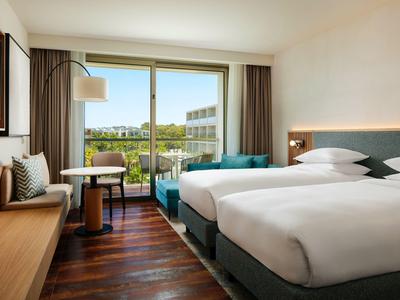 Chambre d'hôtel moderne avec deux lits simples, balcon et vue sur la ville.