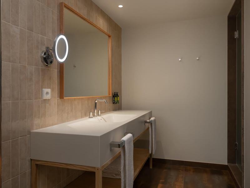 Salle de bain d'hôtel moderne avec double lavabo, grand miroir et sol en bois.