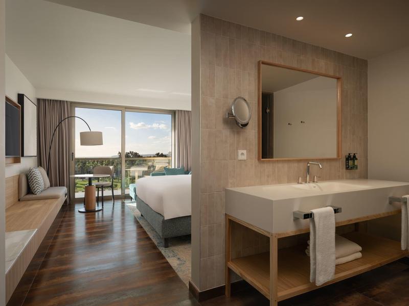 Chambre d'hôtel moderne avec lit double, coin salon, grand miroir et mobilier en bois élégant