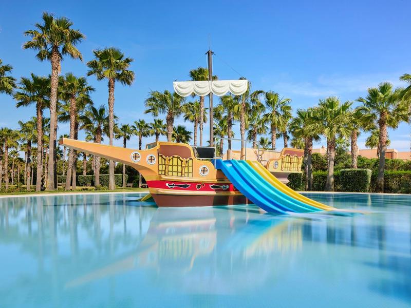 Aire de jeux pour enfants en forme de bateau pirate avec toboggans bleus dans la piscine près des palmiers