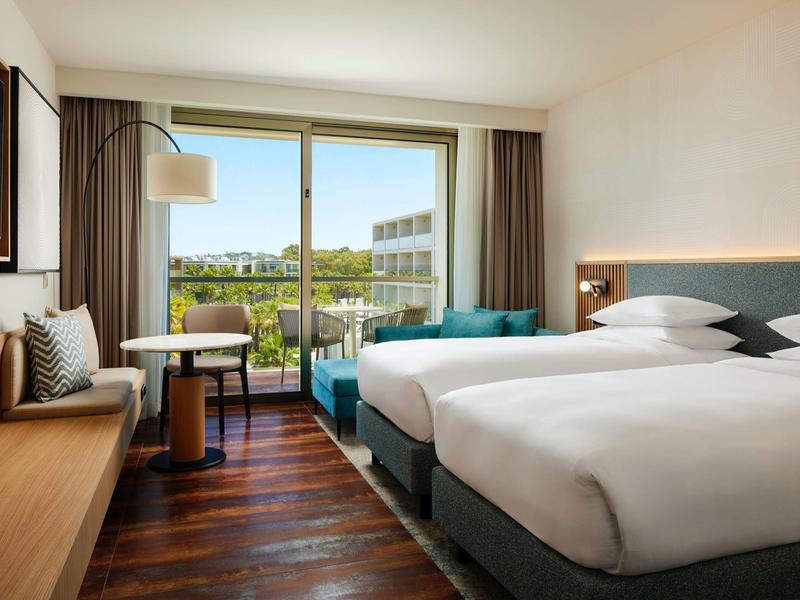 Chambre d'hôtel moderne avec deux lits simples, balcon et vue sur la ville.