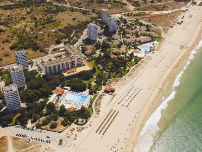 Luftaufnahme eines Strandresorts mit Sandstrand, mehreren Pools und Hochhäusern am Meer.