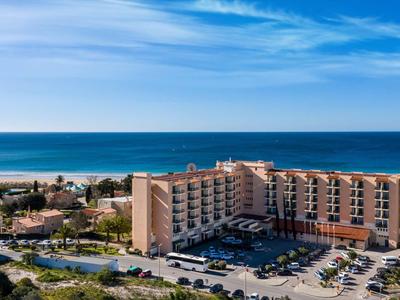 Großes Hotelgebäude neben Strand mit blauem Himmel und Meer im Hintergrund.