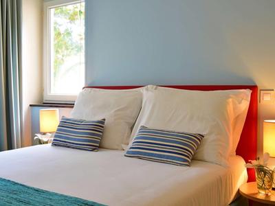 Helles Schlafzimmer mit zweisitzigem Bett, gestreiften Kissen, zwei Nachttischlampen und Fenster.