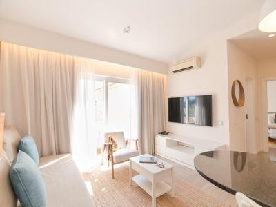 Helles Wohnzimmer mit Sofa, Fernseher und großem Fenster mit Vorhängen.