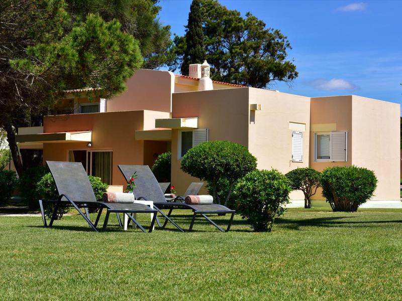 Modernes Ferienhaus mit Liegestühlen und gepflegtem Rasen unter blauem Himmel.