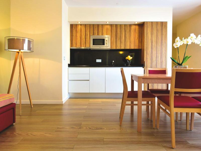 Moderner Essbereich mit Holzboden, roten Stühlen und Küchenzeile im Hintergrund.