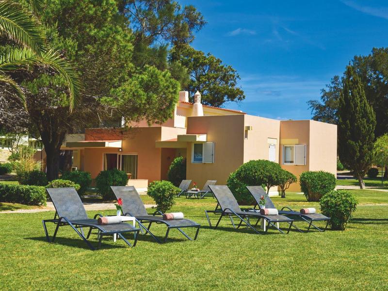 Haus mit Liegestühlen auf grünem Rasen unter blauem Himmel.