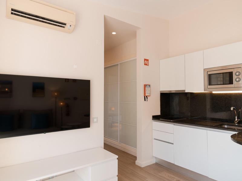 Moderne Küchenecke mit weißen Schränken, Mikrowelle, Spüle und großem Flachbildfernseher an der Wand.