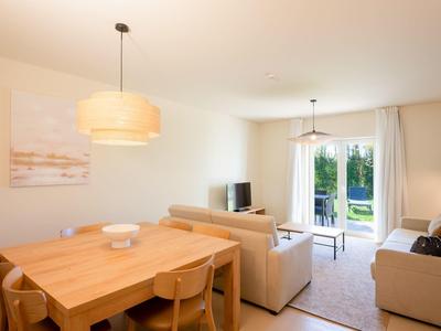 Moderner Wohn- und Essbereich mit Holztisch, beigen Sofas und Zugang zu Balkon mit Blick ins Grüne.