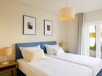 Modernes Schlafzimmer mit zwei Einzelbetten, Nachttischen und Zugang zum Garten.