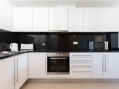 Moderne Hotelküche mit weißen Schränken, schwarzen Arbeitsflächen und Geräten wie Ofen und Mikrowelle.