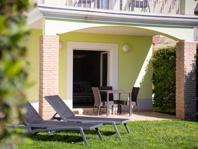 Terrasse mit Gartenmöbeln und Liegestühlen vor einem hellgrünen Haus mit Rasen