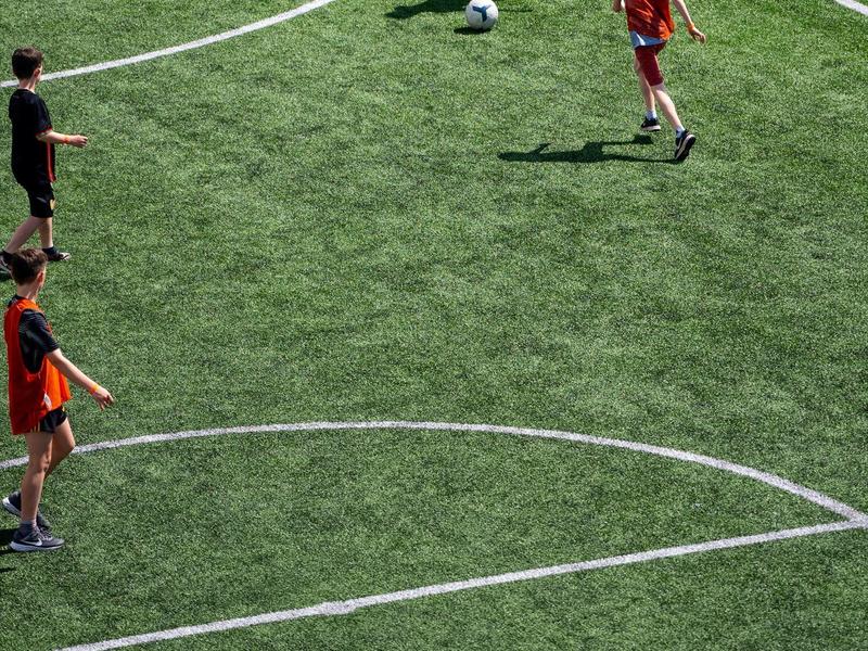 Vier Jungen spielen Fußball auf grünem Kunstrasen mit weißen Spielfeldlinien.