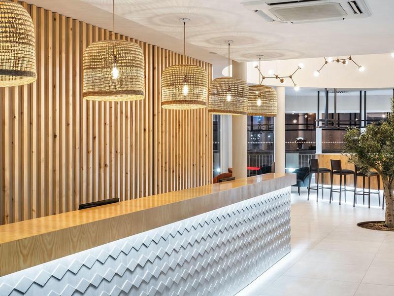 Moderner Empfangsbereich mit Holzpaneelen, Theke mit Beleuchtung und Pflanzen im hellen Raum.