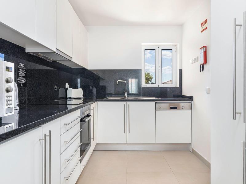 Moderne weiße Küche mit schwarzen Arbeitsplatten, Backofen, Mikrowelle und Fenster für Tageslicht.