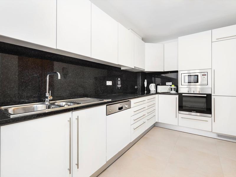 Moderne weiße Küche mit schwarzer Arbeitsplatte, Edelstahlspüle, Ofen und Mikrowelle in Ecke.