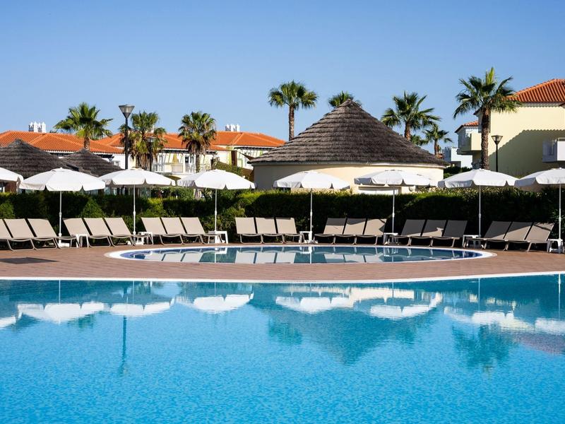 Großer blauer Swimmingpool mit Liegestühlen, weißen Sonnenschirmen und Palmen im Hintergrund.