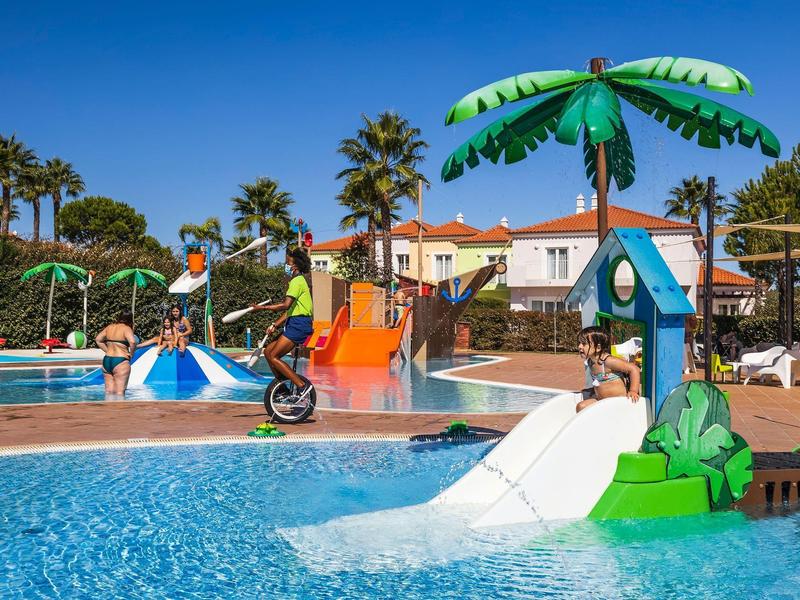 Bunter Kinderspielplatz mit Rutschen und Wasserattraktionen in einem Schwimmbad bei sonnigem Wetter.