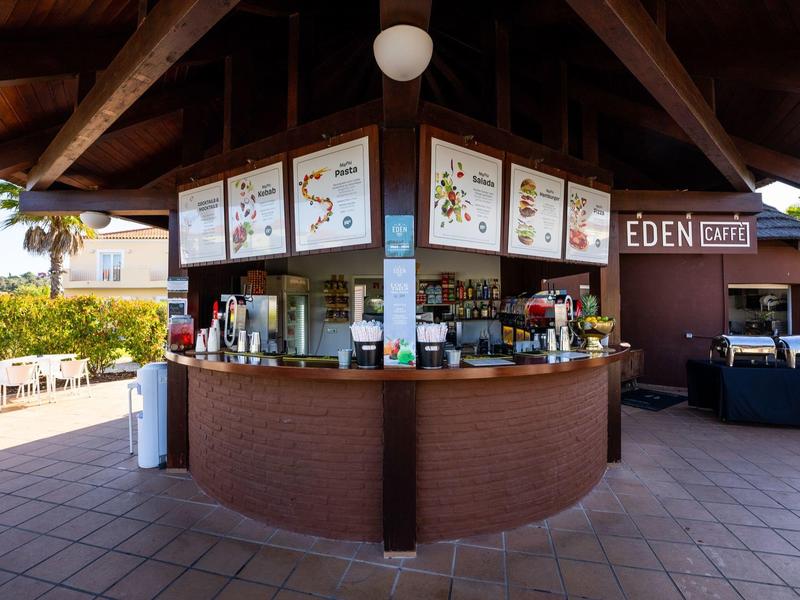 Kleiner Kiosk mit braunem Holz und weißen Schildern unter einem Holzdach auf Terrasse.