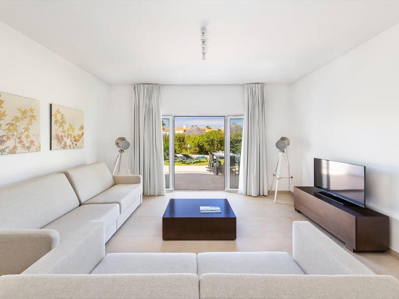 Helles Wohnzimmer mit weißen Wänden, zwei Sofas, zwei Stehlampen, Couchtisch und TV-Schrank vor Terrasse.