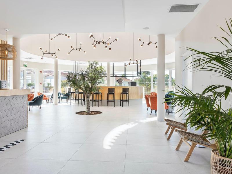 Heller, moderner Innenraum mit großen Fenstern, grünen Pflanzen und Sitzbereich mit Holzmöbeln.